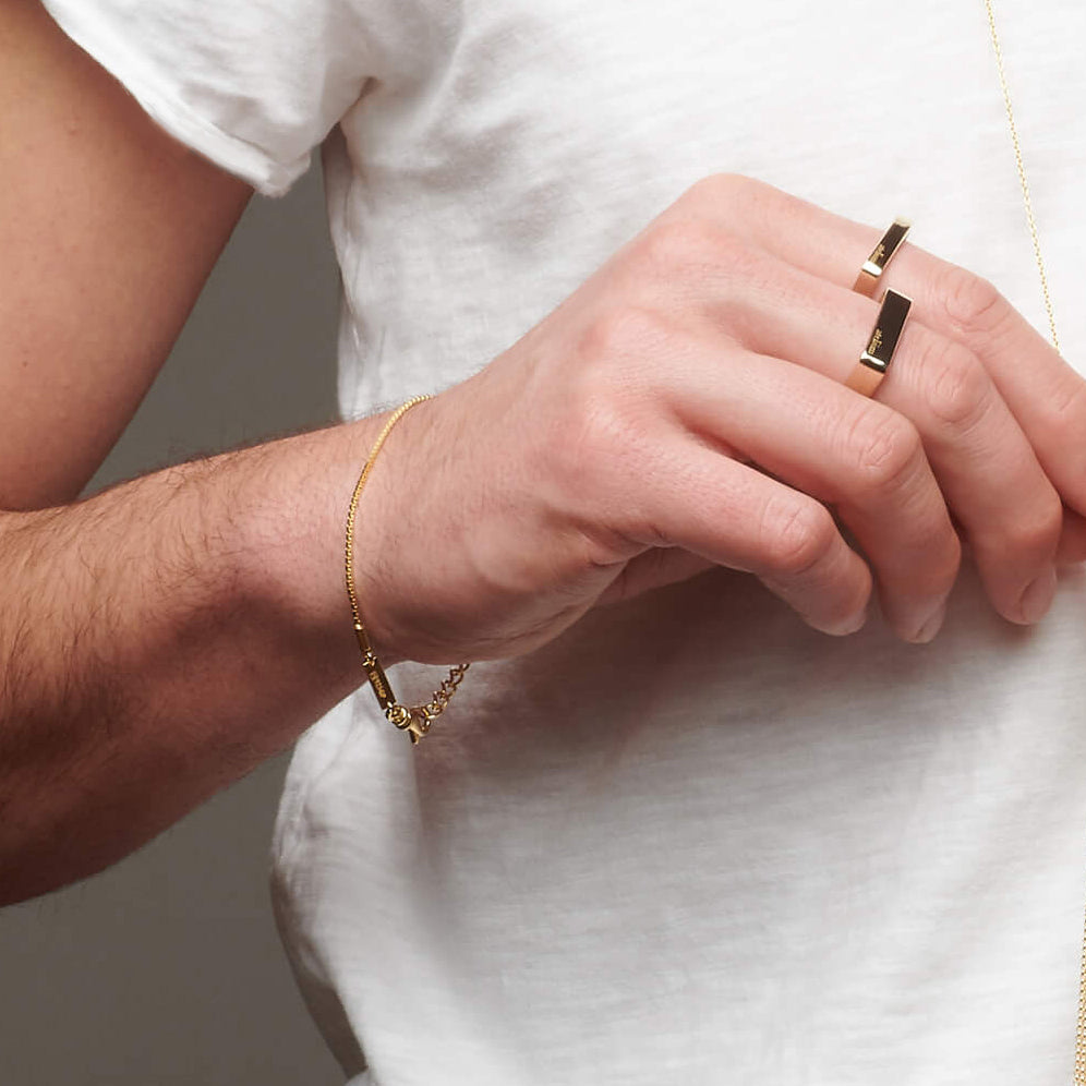 Up close picture of man's wrist with gold atelium bracelet and gold rings