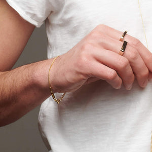 Up close picture of man's wrist with gold atelium bracelet and gold rings