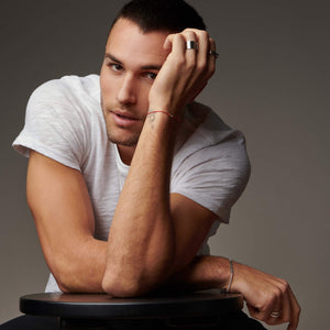 Man sitting with head resting in hand wearing atelium rings and bracelet