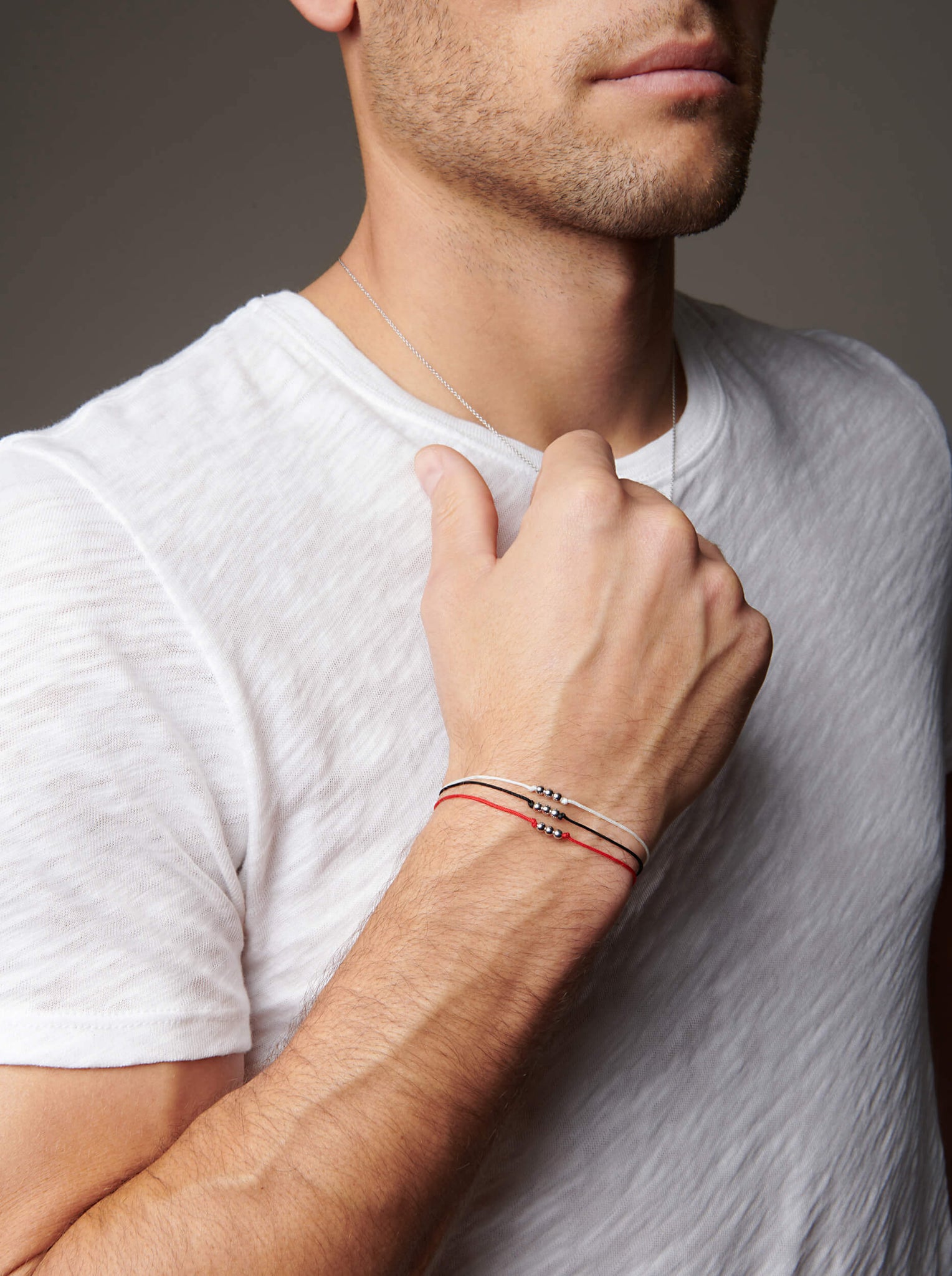 Arm bent towards face with wrist facing outward wearing string bracelets
