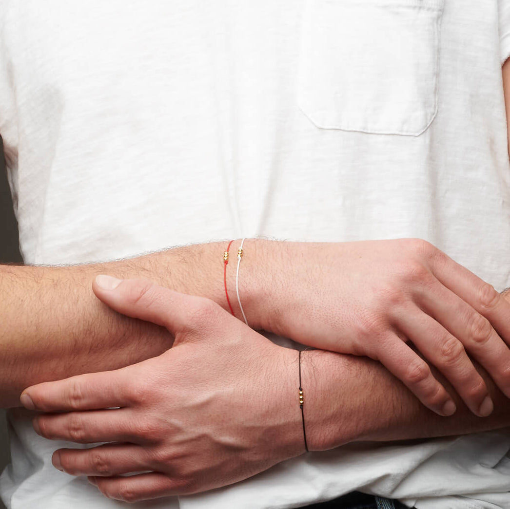 Hands grasping forearms with string bracelets
