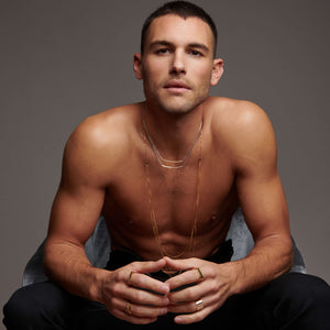 Muscular man sitting facing forward wearing atelium layered necklace and multiple rings  